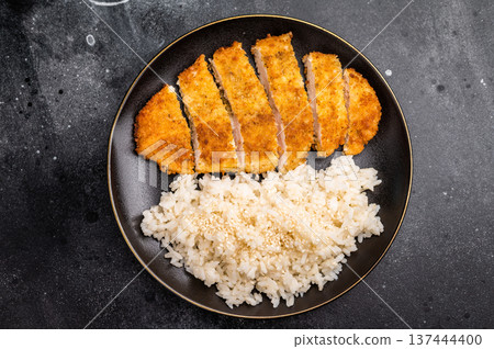 Delicious katsu style dish, featuring a perfectly cooked chicken meat cutlet served alongside steamed rice for a balanced meal. black background. top view Delicious katsu style dish, featuring a perfectly cooked chicken meat cutlet served alongside steamed rice for a balanced meal. black background. top view 137444400