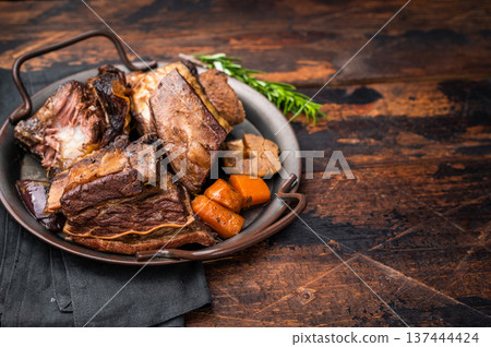 Grilled beef short ribs glistening under natural light, accompanied by fresh greens and spices, capturing the essence of gourmet comfort food. wooden background. top view 137444424