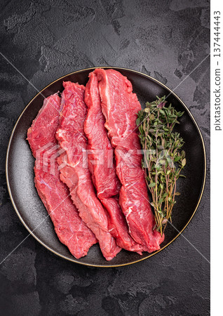 Raw sliced horse meat steaks presented with herbs and spices, inviting creativity in the kitchen for those seeking bold flavors and unique dining experiences. black background. top view Raw sliced horse meat steaks presented with herbs and spices, inviting creativity in the kitchen for those seeking bold flavors and unique dining experiences. black background. top view 137444443