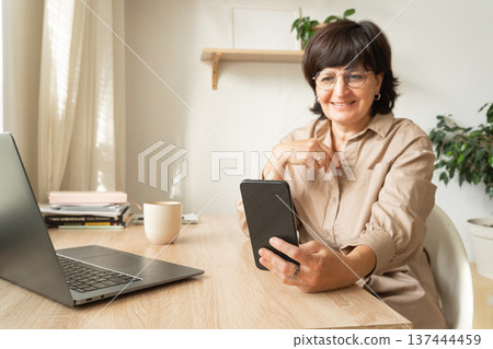 Mature woman smiling having video call on smartphone Mature woman smiling having video call on smartphone 137444459