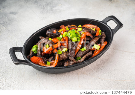 Beef stir fry with peppers and green onion cooked in skillet. Chinese pepper steak inspired beef strips dish on light background. Beef stir fry with peppers and green onion cooked in skillet. Chinese pepper steak inspired beef strips dish on light background. 137444479