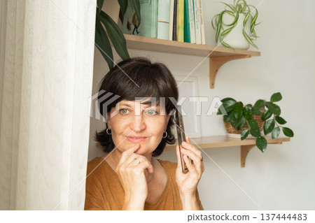 Caucasian mature female relaxing at home with smartphone among indoor plants Caucasian mature female relaxing at home with smartphone among indoor plants 137444483