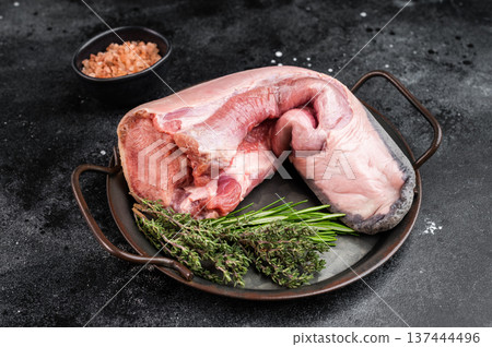 Raw beef tongue on plate with herbs and pink salt on dark background. Traditional organ meat ingredient with copy space. Raw beef tongue on plate with herbs and pink salt on dark background. Traditional organ meat ingredient with copy space. 137444496