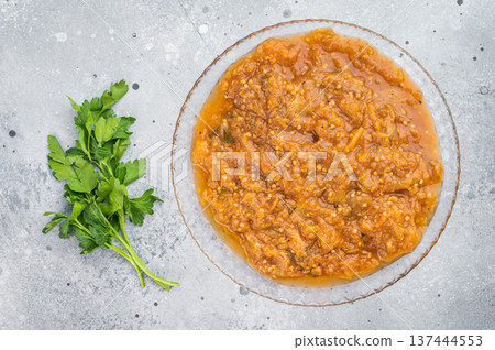 Traditional roasted eggplant dip melitzanosalata inspired vegetable relish presented in transparent plate overhead on light concrete background 137444553