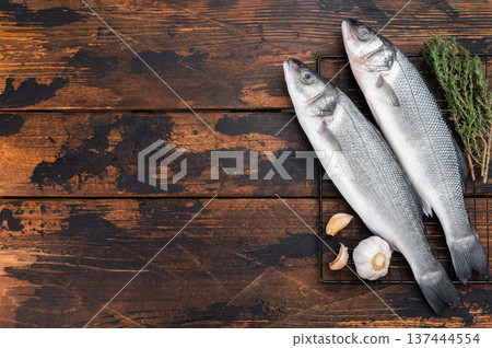 Two whole raw sea bass fish with thyme and garlic on rustic wooden background, fresh Mediterranean seafood ingredient for healthy gourmet cooking concept. 137444554