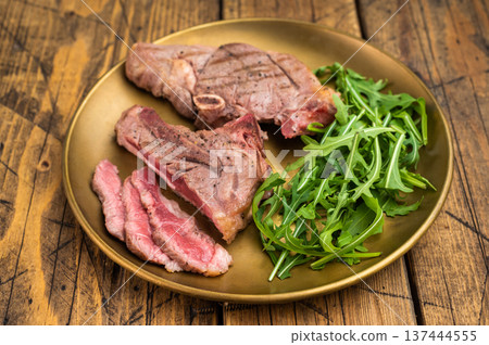BBQ grilled lamb rump steak with bone, juicy medium rare slices and green salad leaves. top view, wooden background 137444555