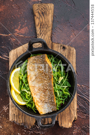 Fried Zander style fish fillet served in cast iron pan with arugula salad and lemon slices, mediterranean seafood dish photographed from above. 137444558