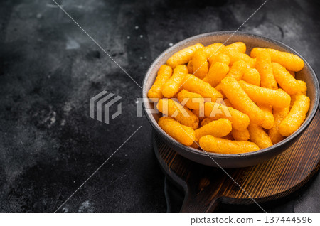 Deliciously addictive cheese flavored corn puffs, beautifully arranged on a plate. black background. top view Deliciously addictive cheese flavored corn puffs, beautifully arranged on a plate. black background. top view 137444596