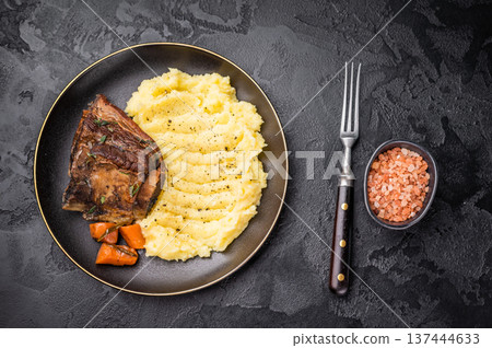Braised beef short ribs resting on a bed of creamy mashed potatoes, creating an inviting culinary scene. black background. top view 137444633