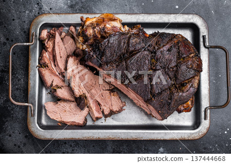 Roast Venison leg, baked meat of roe deer with bone on a tray with herbs. black background. top view 137444668