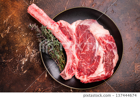 Fresh Tomahawk beef steak, raw marbled rib eye with bone on plate with herbs. brown background. top view Fresh Tomahawk beef steak, raw marbled rib eye with bone on plate with herbs. brown background. top view 137444674