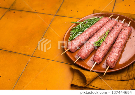 Raw Turkish Urfa kebab skewers on a plate with herbs. orange background. top view 137444694