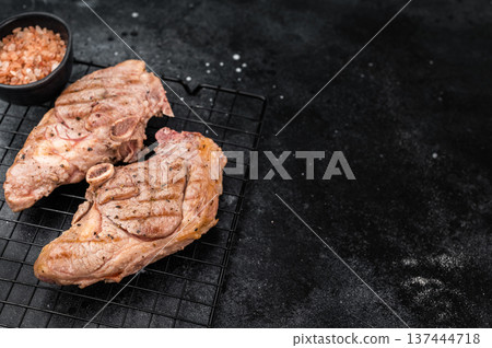 BBQ roasted lamb sirloin chops with bone placed on metal rack, seared surface with spices and pepper, gourmet grilled meat top view composition. 137444718