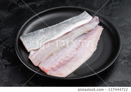 Uncooked European sea bass fillet on black plate , clean culinary layout ideal for seafood menu, cooking recipe or nutrition design. 137444722