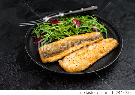 Pan fried sea bass fillets served on black plate with fresh arugula salad, gourmet seafood meal on black background with copy space. 137444732