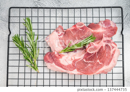 Raw lamb chump chops with bone placed on cooling rack with fresh rosemary, premium sirloin saddle meat prepared for roasting, grilling or gourmet cooking. 137444735