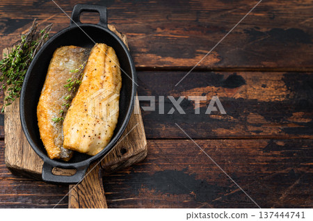 Crispy fried sea bass fish fillet with thyme in cast iron pan, mediterranean seafood dinner composition with rustic wooden background and copy space. 137444741