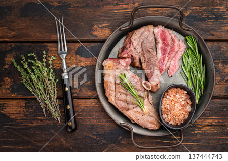 Grilled lamb chump chop with medium rare slices, rosemary and pink salt served on rustic pan, gourmet meat presentation in overhead view. 137444743