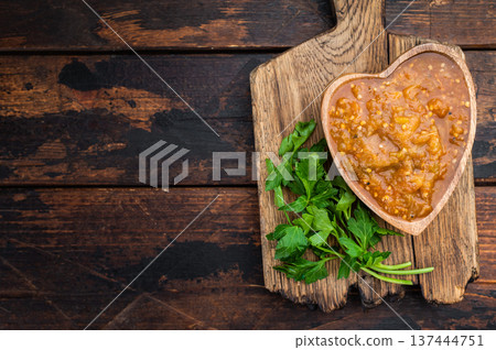 Traditional eggplant caviar style spread with rich texture and parsley garnish placed on wooden cutting board over dark rustic table top view composition 137444751
