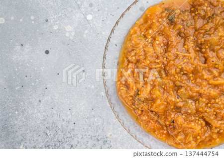 Traditional roasted eggplant dip melitzanosalata inspired vegetable relish presented in transparent plate overhead on light concrete background Traditional roasted eggplant dip melitzanosalata inspired vegetable relish presented in transparent plate overhead on light concrete background 137444754