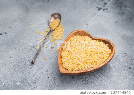 Raw Orzo pasta, uncooked dry Italian risoni in a bowl. grey background. top view Raw Orzo pasta, uncooked dry Italian risoni in a bowl. grey background. top view 137444845