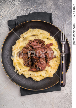 German Braised Beef Cheek, Slow cooked meat with smashed potatoes on a plate. grey background. top view 137444874