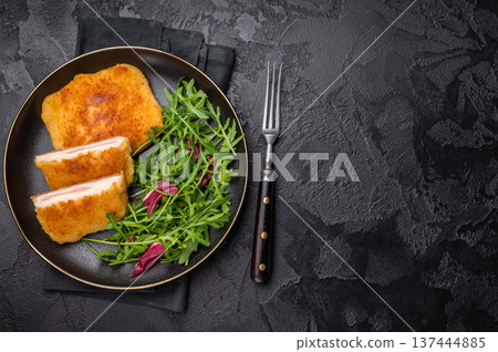 Chicken cordon bleu cutlet with cheese and ham on plate with salad. black background. top view 137444885
