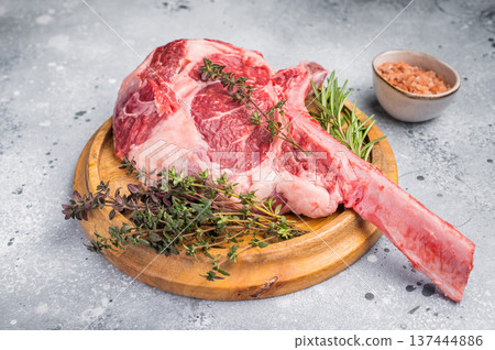 Uncooked tomahawk steak, raw black angus beef rib eye with bone on wooden board. grey background. top view 137444886