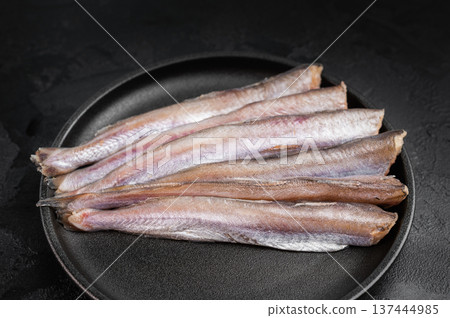 Fresh raw Putassu blue whiting fish on black plate with thyme and pink salt, minimal dark food styling with copy space, natural marine seafood ingredient ready for cooking 137444985
