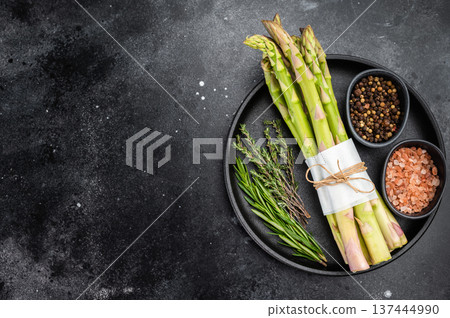 Fresh green asparagus bundle with rosemary, thyme and spices on black plate, dark rustic background with copy space, organic vegan ingredient concept 137444990
