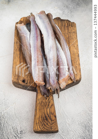 Raw blue whiting fish resembling small hake or codling on rustic wooden board with thyme and pepper, minimal seafood composition on light textured background 137444993