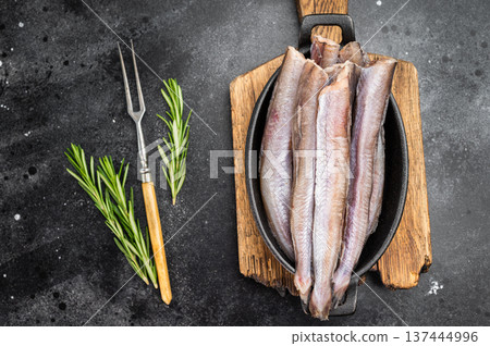 Fresh silver blue whiting fillets in rustic pan on black background, marine catch resembling pollock or small hake, simple preparation and gourmet seafood concept 137444996
