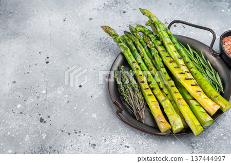 Roasted asparagus spears with grill marks and herbs on minimal grey backdrop, gourmet vegetarian side dish in modern food styling. 137444997