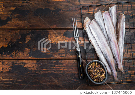 Raw blue whiting fish prepared on rustic wooden background with fork and pepper, fresh marine seafood ingredient similar to whiting, hake and pollock, natural copy space 137445000