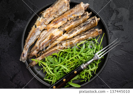 Fried blue whiting fish served with fresh arugula on dark textured background, healthy seafood meal with copy space and minimal styling Fried blue whiting fish served with fresh arugula on dark textured background, healthy seafood meal with copy space and minimal styling 137445010