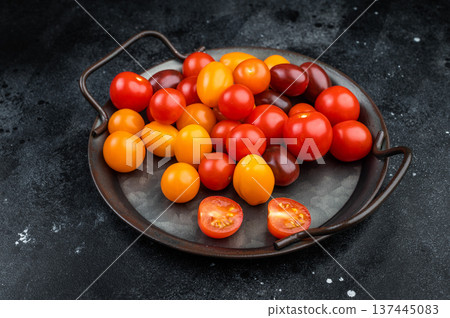 Assorted heirloom cherry tomatoes whole and sliced on a rustic metal dish over a black background ideal for healthy food concepts. 137445083
