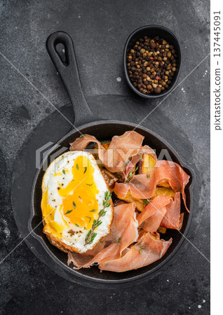 Huevos rotos con jamon with fried potatoes and runny egg cooked in cast iron skillet top view on dark stone background 137445091