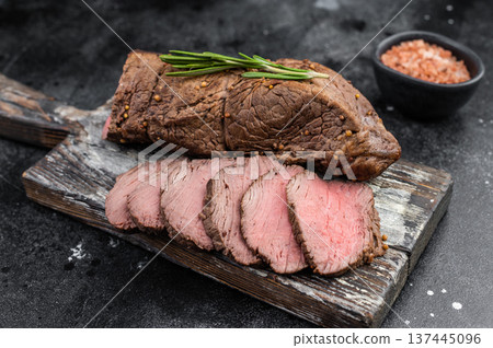 Gourmet roasted beef tenderloin sliced and served with rosemary salt and knife on dark textured background copy space 137445096