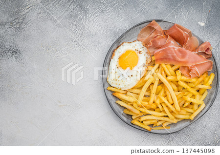 Spanish huevos rotos con jamon with fries and sunny egg yolk on ceramic plate overhead copy space 137445098