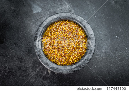 Traditional Dijon mustard with rich grainy texture prepared in stone mortar rustic food styling on dark background 137445100