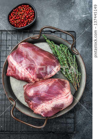 Whole lamb mutton hearts with visible muscle fibers placed on metal plate with thyme and peppercorns for authentic food styling. 137445149