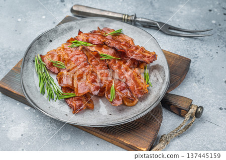 Smoked crispy bacon rashers with rich glossy shine styled with herbs on a rustic board offering strong appetizing food appeal.. Smoked crispy bacon rashers with rich glossy shine styled with herbs on a rustic board offering strong appetizing food appeal.. 137445159