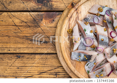 Marinated salted herring fish pieces with spices on round wooden board. Nordic preserved seafood top view with copy space. 137445166