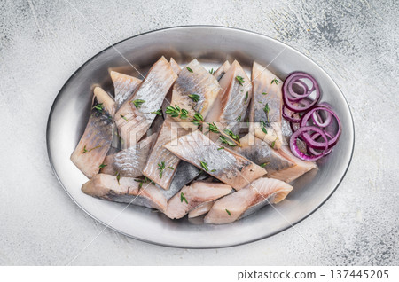 Salted and marinated herring pieces with red onion and thyme served in white dish on wooden board. Light stone background with copy space. 137445205