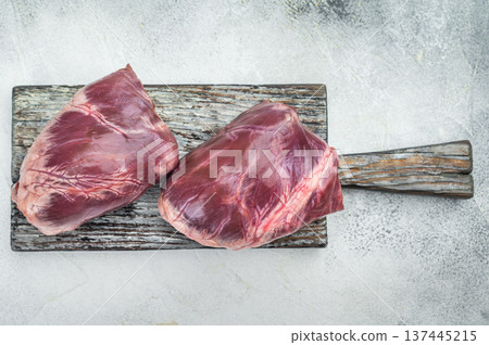 Raw lamb and goat hearts on rustic cutting board with visible muscle fibers fascia and natural texture beside rosemary and pepper. Raw lamb and goat hearts on rustic cutting board with visible muscle fibers fascia and natural texture beside rosemary and pepper. 137445215