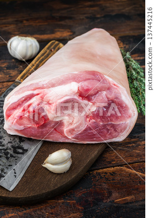 Raw pork knuckle with forged cleaver garlic and thyme on rustic wooden background perfect for butchery themes and recipe imagery. Raw pork knuckle with forged cleaver garlic and thyme on rustic wooden background perfect for butchery themes and recipe imagery. 137445216