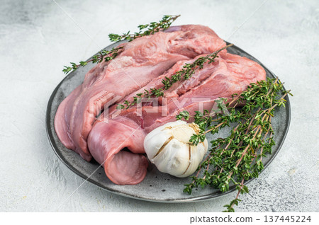 Whole raw uncooked lamb mutton tongue offal arranged on plate with herbs and garlic top view white background. 137445224