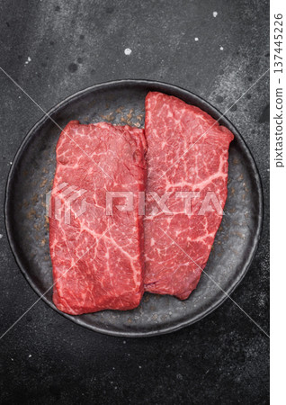 Fresh raw flatiron chuck beef steak with rich marbling on dark ceramic plate overhead view premium flatiron chuck cut for gourmet cooking Fresh raw flatiron chuck beef steak with rich marbling on dark ceramic plate overhead view premium flatiron chuck cut for gourmet cooking 137445226