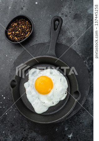 Sunny fried egg cooking in black skillet, crisp edges and glowing yolk. Minimal gourmet breakfast shot with strong texture detail. Sunny fried egg cooking in black skillet, crisp edges and glowing yolk. Minimal gourmet breakfast shot with strong texture detail. 137445258