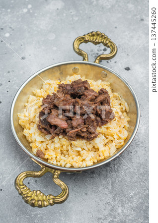 Kawurma qawurma layered over aromatic rice pilaf, highlighting seared protein fibers, granular structure and vintage culinary setup. 137445260